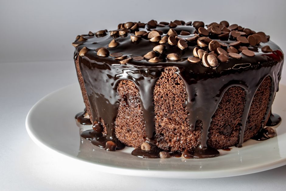 Close-up of a chocolate cake topped with a luscious ganache and chocolate chips on a white plate.